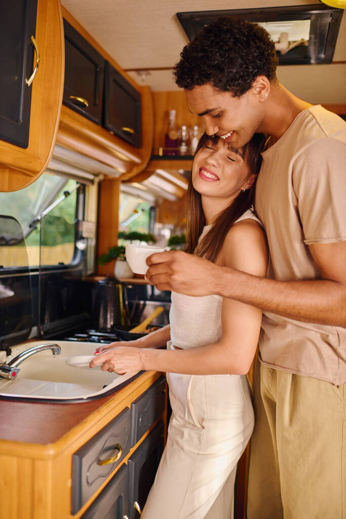 An interracial couple stand side by side in their kitchen, engaging in conversation next to the sink. - Photo, Image