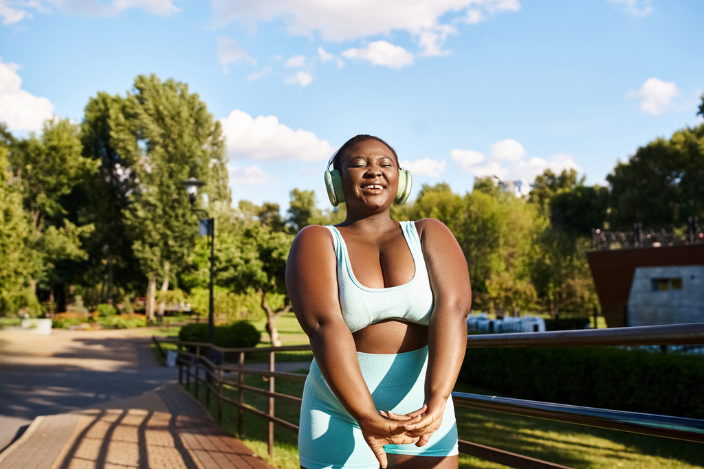 Una mujer afroamericana con los brazos cruzados se para con confianza en un banco, abrazando su fuerza y positividad corporal. - Foto, imagen