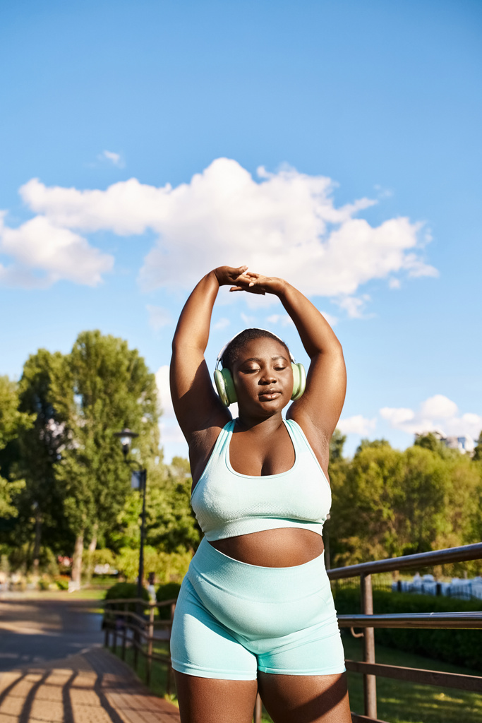 Een Afro-Amerikaanse vrouw traint enthousiast buiten in een blauwe sportbeha en bijpassende korte broek, die lichaamspositiviteit en zelfvertrouwen belichaamt. - Foto, afbeelding