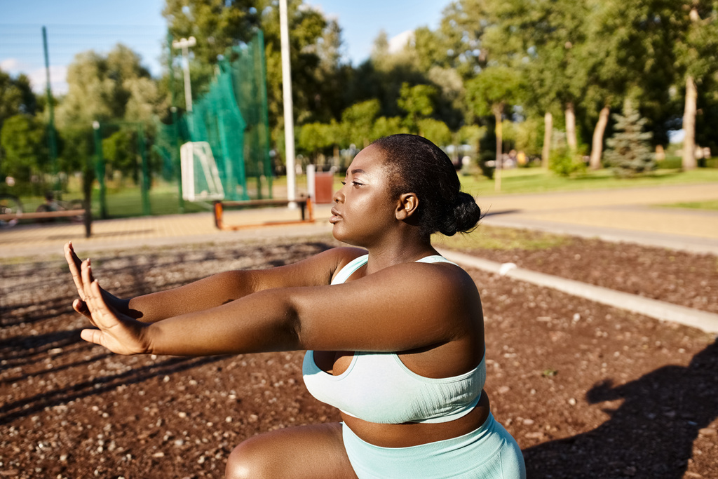 Afroamerykanka w niebieskim staniku sportowym rozciąga ramiona na świeżym powietrzu, obejmując swoje ciało pozytywną i fitness podróż. - Zdjęcie, obraz