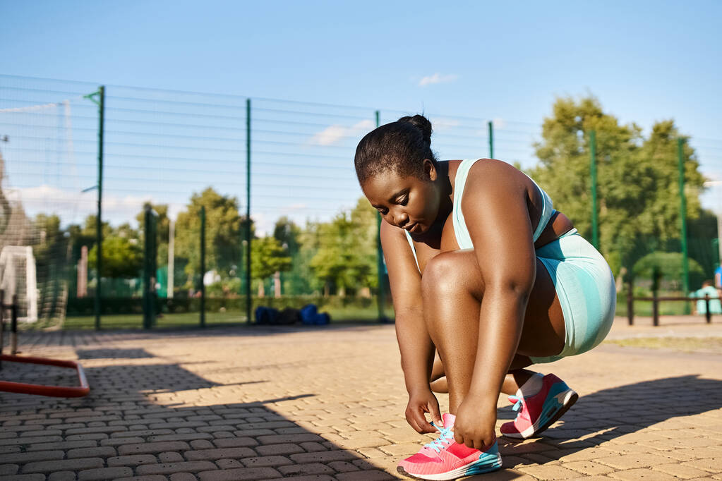 Афро-американка в спортивной одежде демонстрирует свои навыки в сквоте в парке. - Фото, изображение