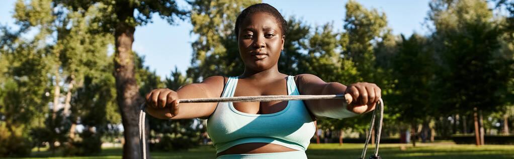 Una donna afroamericana, corpo positivo e forte, solleva una corda da salto in un vivace parco. - Foto, immagini