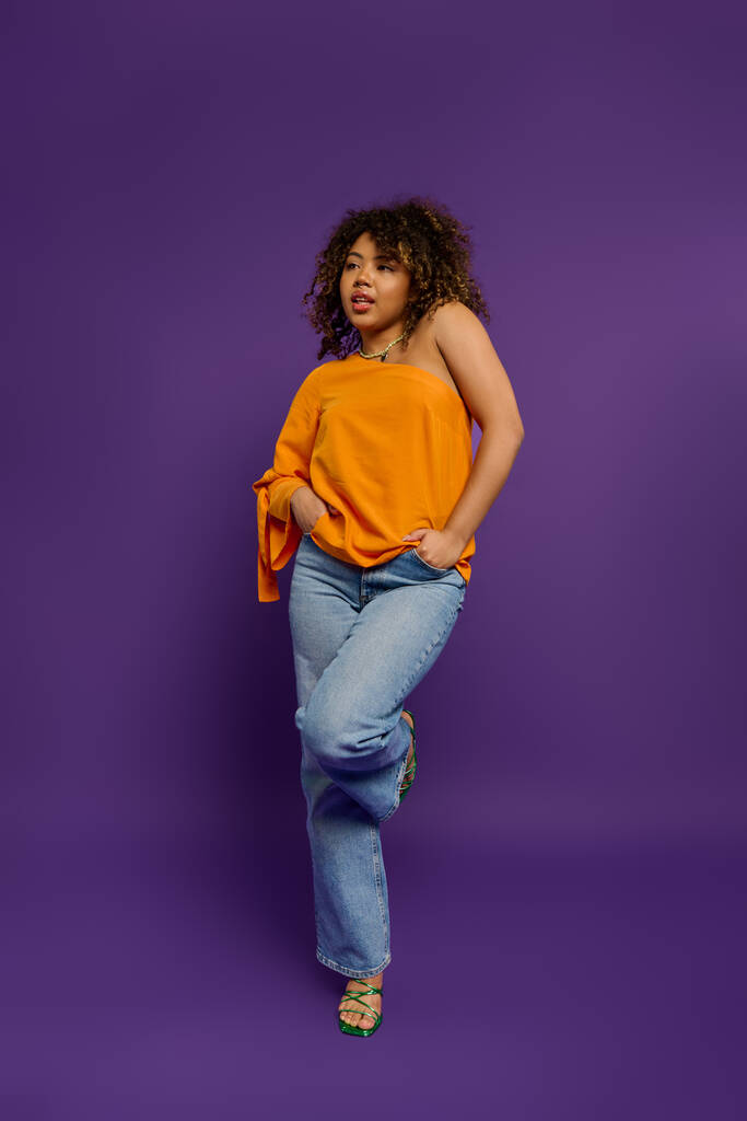 Mujer afroamericana con estilo posa en la vibrante parte superior naranja contra el telón de fondo colorido. - Foto, Imagen