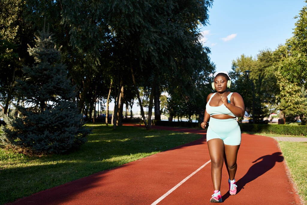 Afrikkalainen amerikkalainen nainen urheiluvaatteissa kulkee päättäväisesti elinvoimaisella punaisella radalla, joka ilmentää voimaa ja urheilullisuutta.. - Valokuva, kuva