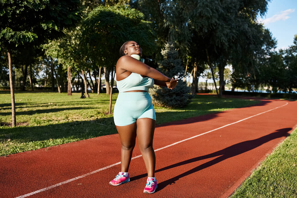 African American woman with a curvy body stands on a track, warming up - Photo, Image