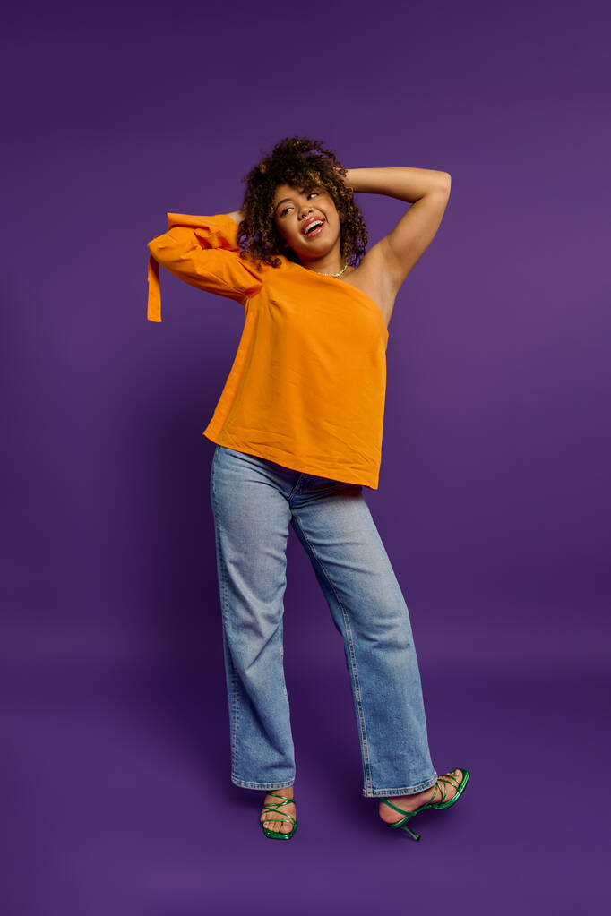 スタイリッシュなアフリカ系アメリカ人女性はオレンジ色のシャツで活気に満ちた背景にポーズします. - 写真・画像
