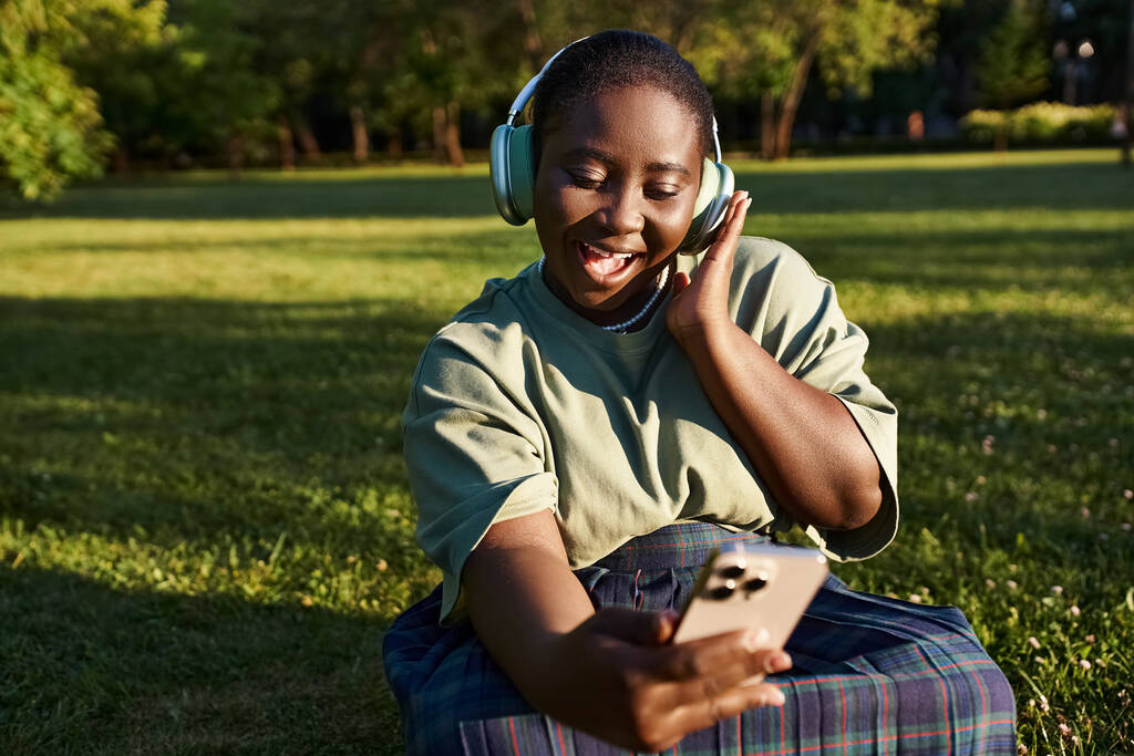 Ένα ξέγνοιαστο νεαρό αγόρι χαλαρώνει στο γρασίδι, ακούγοντας προσεκτικά τη μουσική του, χαμένο στις μελωδίες. - Φωτογραφία, εικόνα