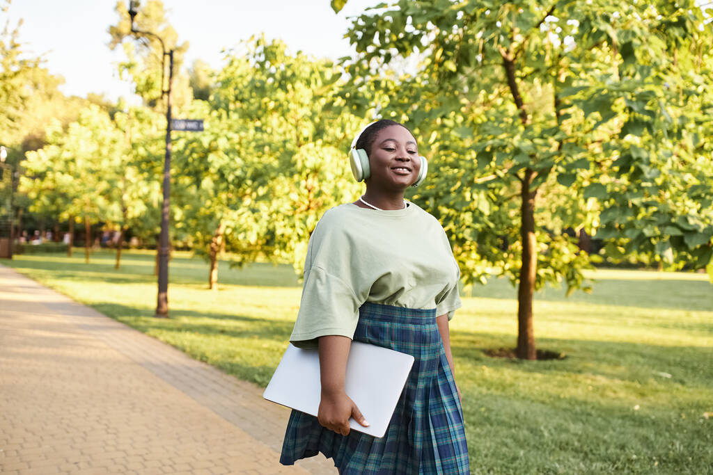 カジュアルな服装のアフリカ系アメリカ人女性が夏に公園の歩道を自信を持って歩きます. - 写真・画像