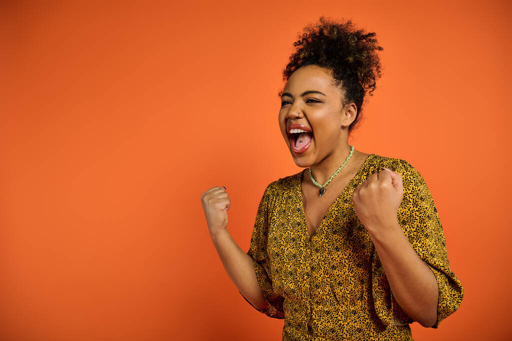 Una hermosa mujer afroamericana con la boca abierta posando sobre un vibrante telón de fondo naranja. - Foto, Imagen