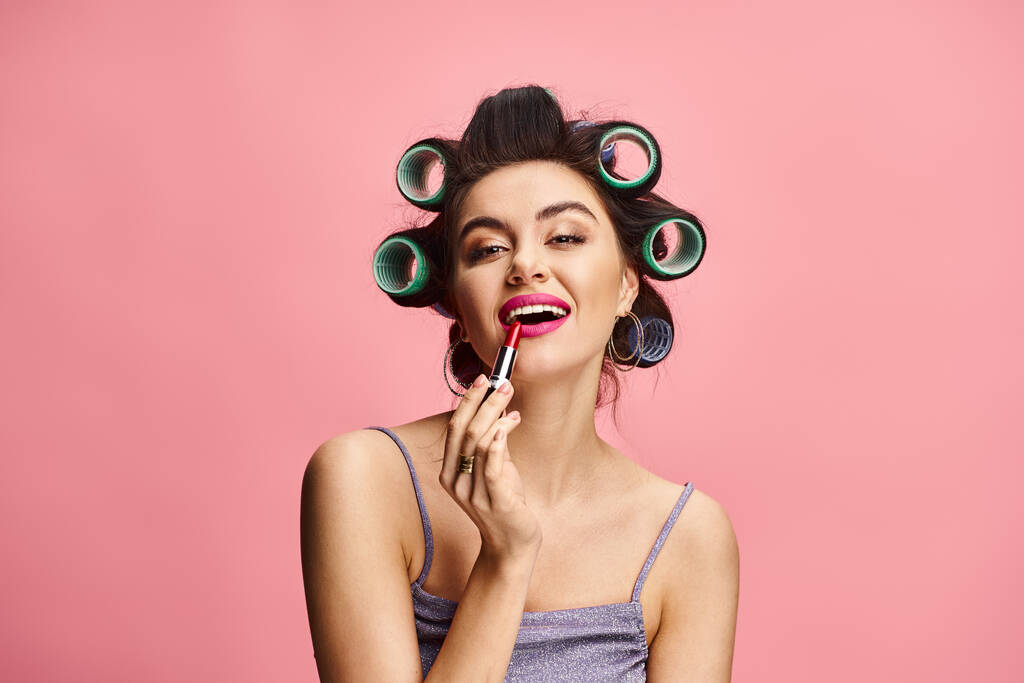 A woman with curlers on her head applying lipstick. - Photo, Image