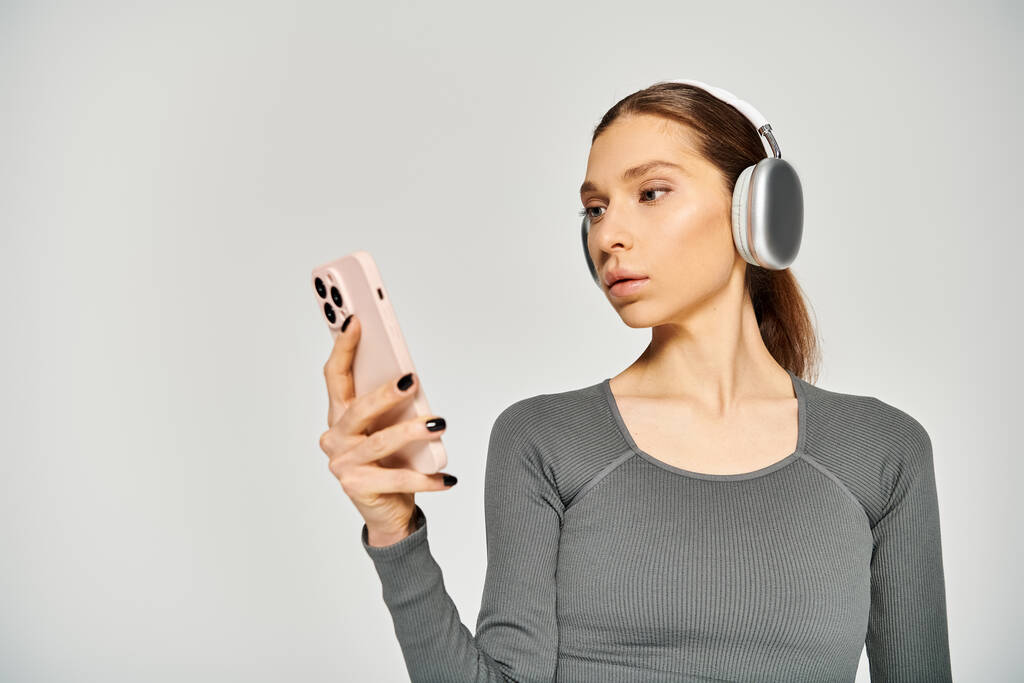 Спортивная девушка в активной одежде слушает музыку в наушниках, держа в руках мобильный телефон. - Фото, изображение