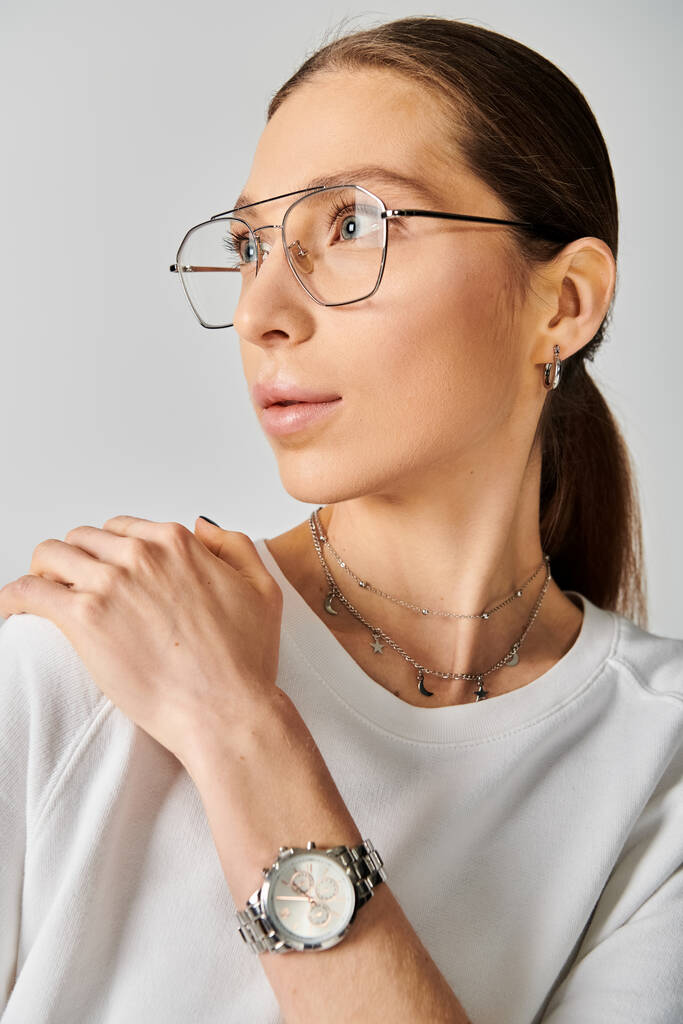 A young woman exudes modern elegance in a white shirt, complemented by stylish glasses, against a neutral grey backdrop. - Photo, Image