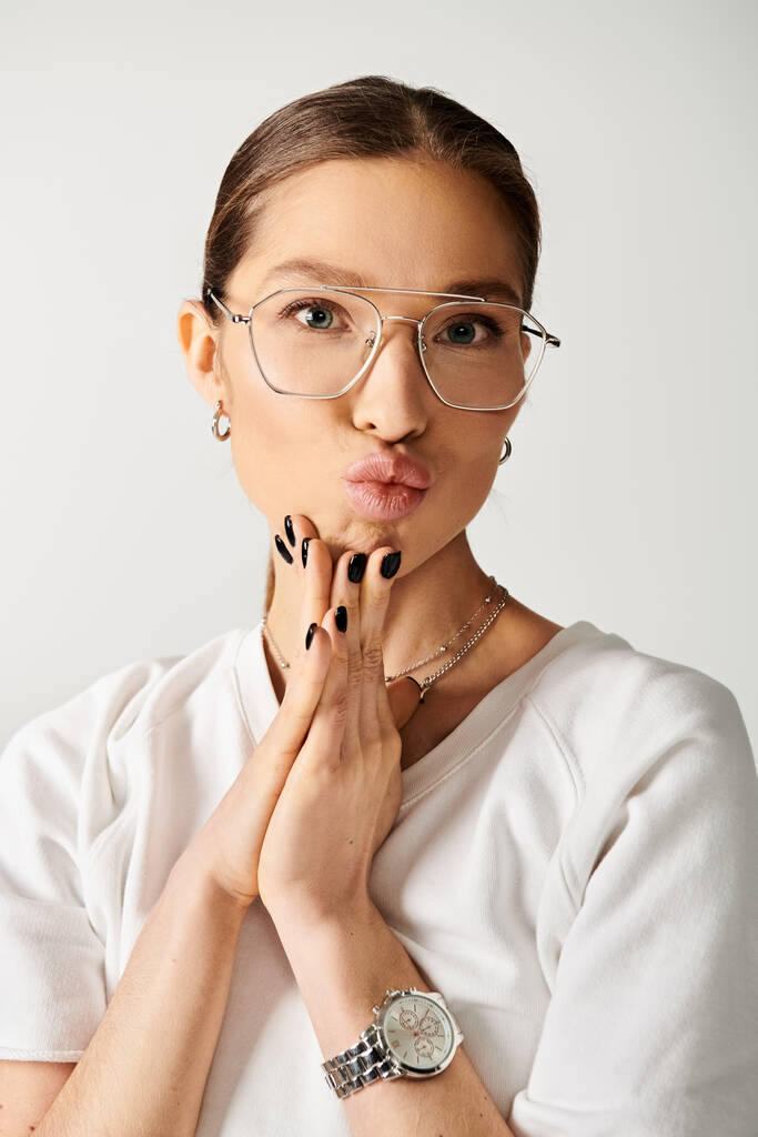 A young woman in a white t-shirt and glasses is making a funny face against a grey background. - Photo, Image