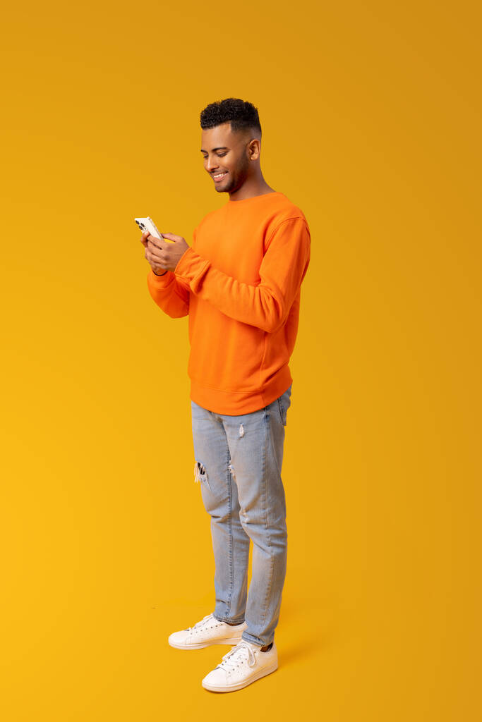 Homem alegre e despreocupado usando smartphone isolado no amarelo, cara passa o lazer em redes sociais, conversando on-line, compras, usando novo aplicativo móvel, comprimento total, vertical - Foto, Imagem