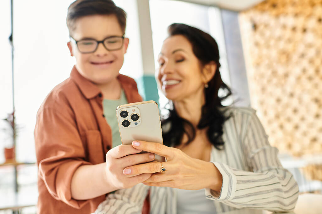 centrarse en el teléfono inteligente moderno en manos de madre alegre borrosa y su hijo inclusivo con síndrome de Down - Foto, Imagen
