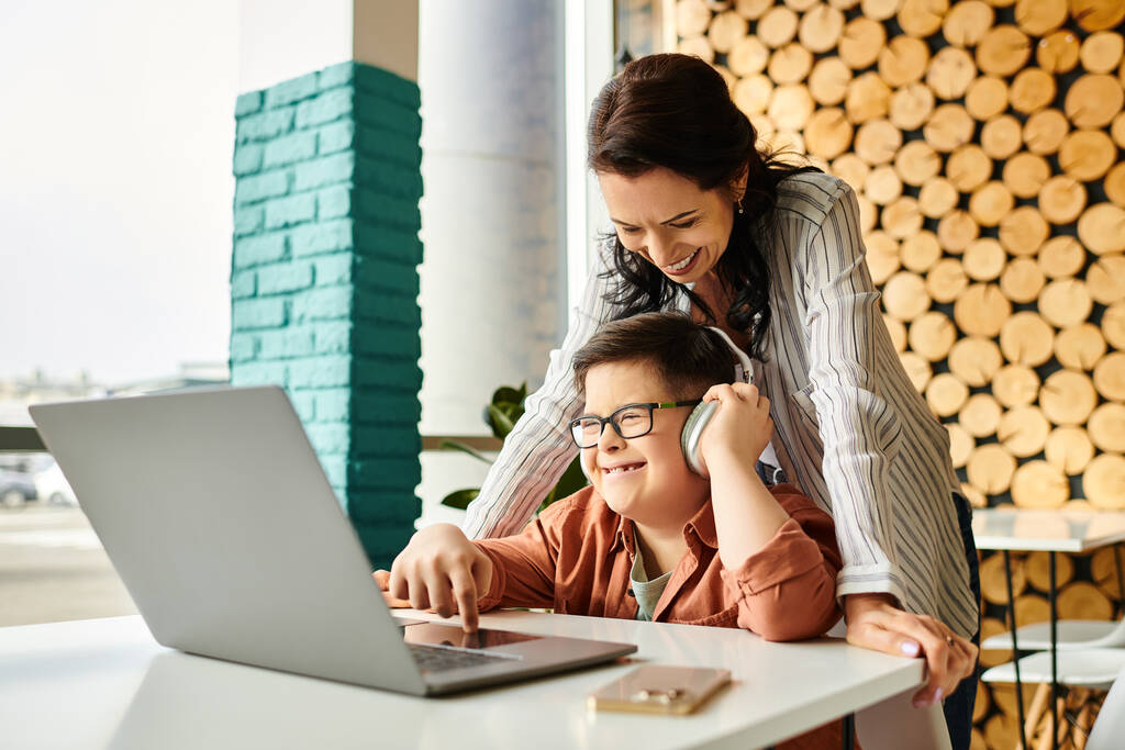 alegre madre pasar tiempo con su hijo con síndrome de Down en la cafetería mientras juega en el ordenador portátil - Foto, Imagen