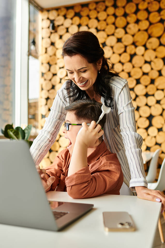 hilpeä äiti viettää aikaa poikansa kanssa Downin oireyhtymä kahvilassa, kun hän pelaa kannettavalla tietokoneella - Valokuva, kuva
