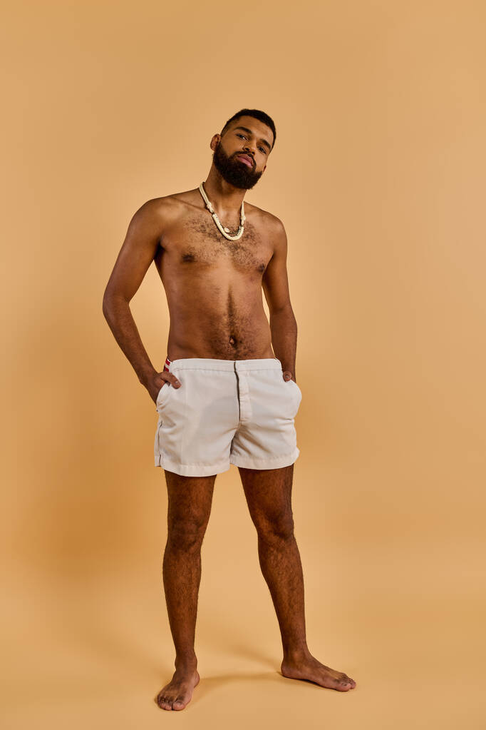 Un uomo senza camicia in piedi con fiducia di fronte a uno sfondo abbronzato, mostrando il suo fisico muscolare e il senso di sicurezza di sé. - Foto, immagini
