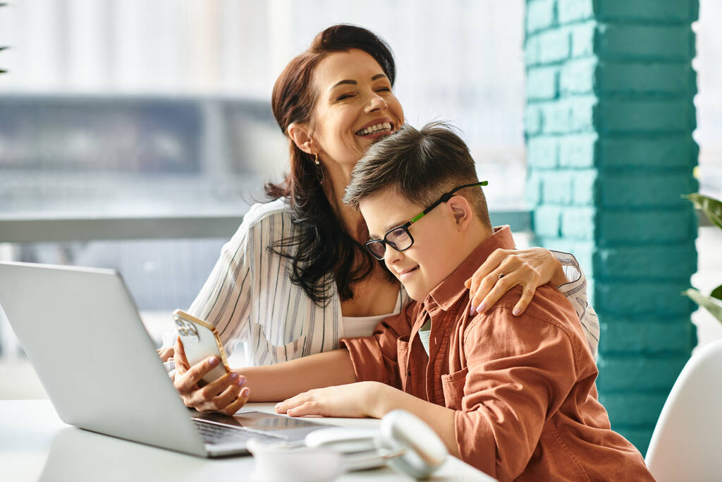 schattig inclusieve jongen met Down syndroom tijd doorbrengen met zijn vrolijke moeder in de voorkant van laptop - Foto, afbeelding