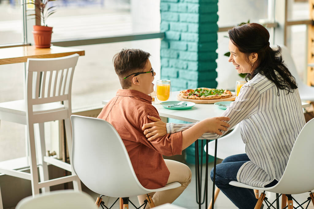 Schöne Mutter isst Pizza und trinkt Saft mit ihrem netten Sohn mit Down-Syndrom - Foto, Bild