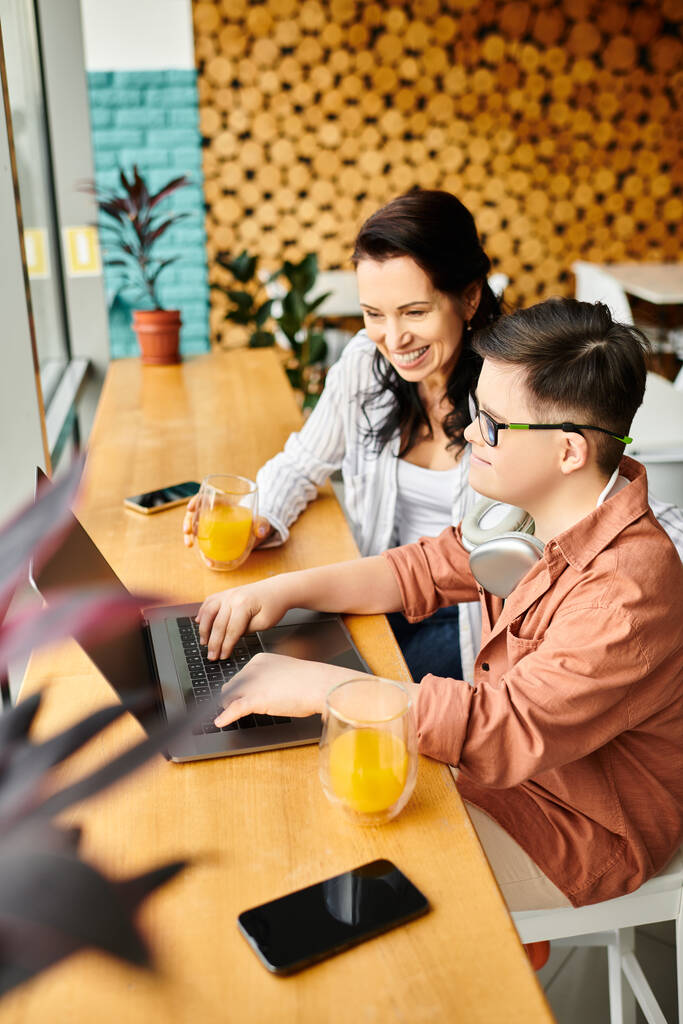 радісний хлопчик з синдромом Дауна з навушниками, що грають на ноутбуці поруч зі своєю матір'ю в кафе - Фото, зображення