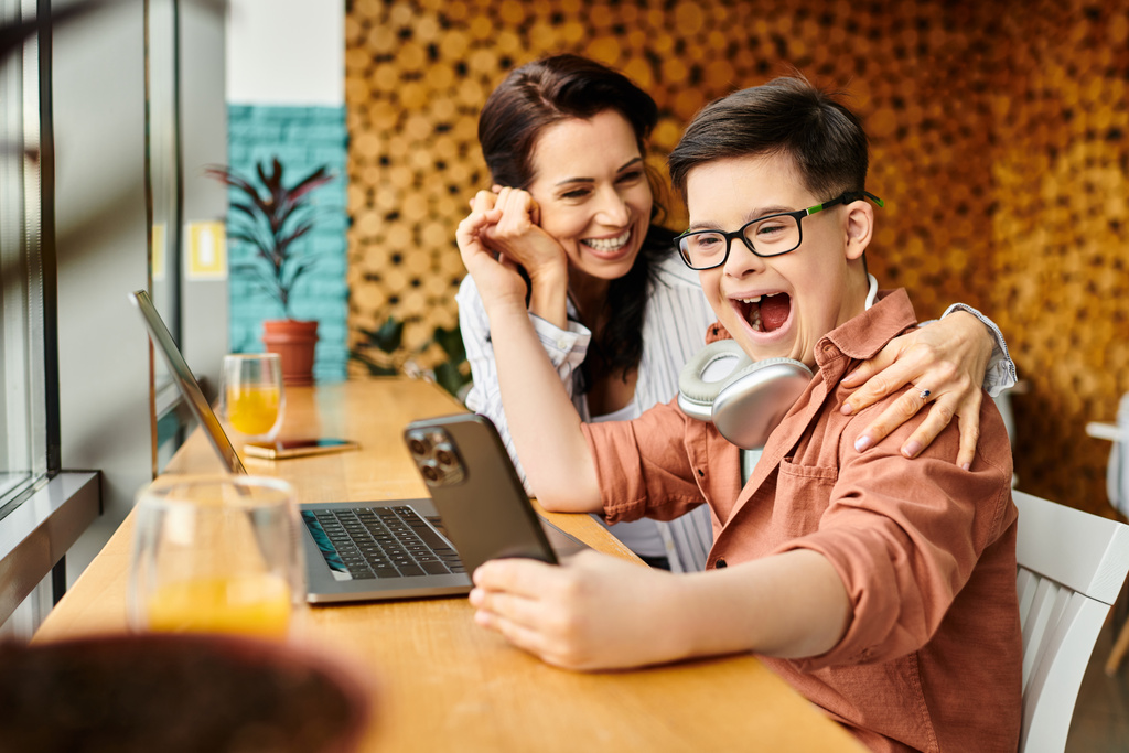 веселий хлопчик з синдромом Дауна дивиться на смартфон біля своєї веселої матері в кафе - Фото, зображення