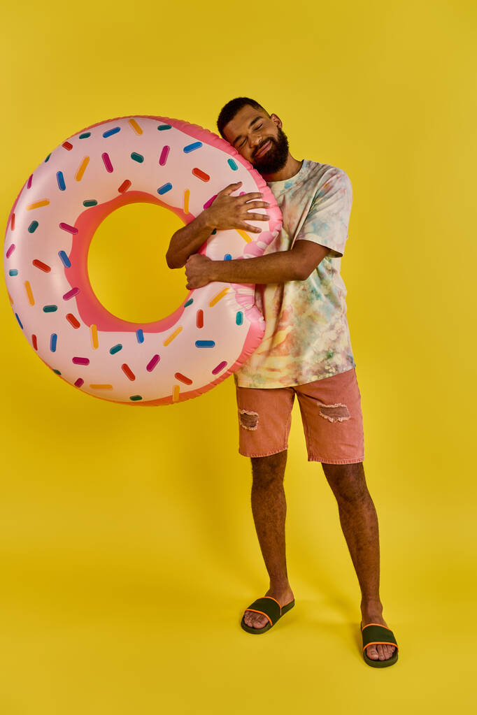 Ein Mann hält freudig einen riesigen Donut vor einem leuchtend gelben Hintergrund und zeigt damit seine Liebe für die süße Leckerei.. - Foto, Bild