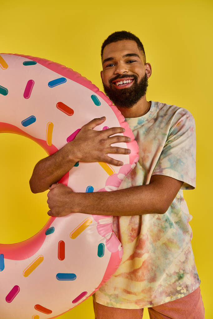 Ein Mann unbekannten Alters hält einen riesigen, köstlich aussehenden Donut vor einem leuchtend gelben Hintergrund. - Foto, Bild
