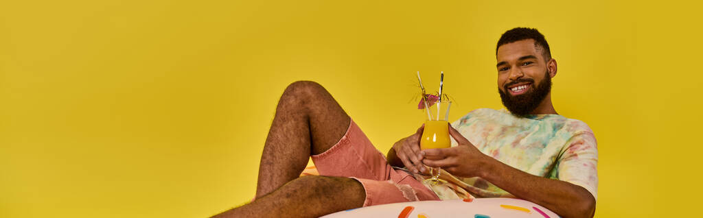 Un hombre con gracia se sienta en una colorida pelota de playa, disfrutando tranquilamente de una copa de vino en un entorno sereno de playa. - Foto, imagen