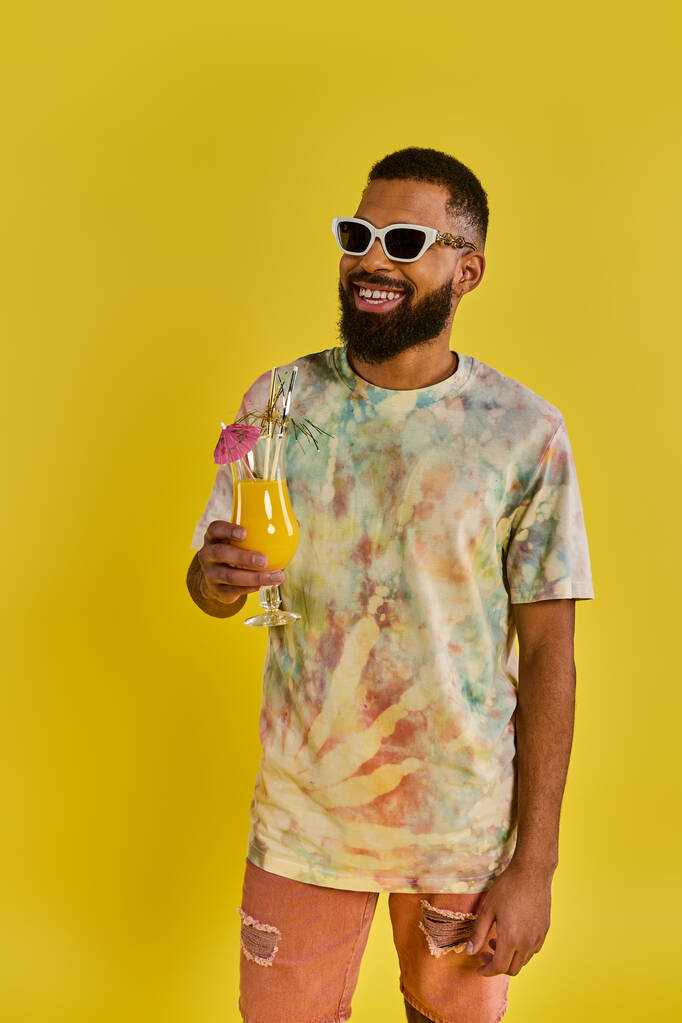 Un hombre con estilo en una camisa de tinte de corbata es pausado sosteniendo una bebida, exudando un ambiente relajado y de espíritu libre. - Foto, imagen