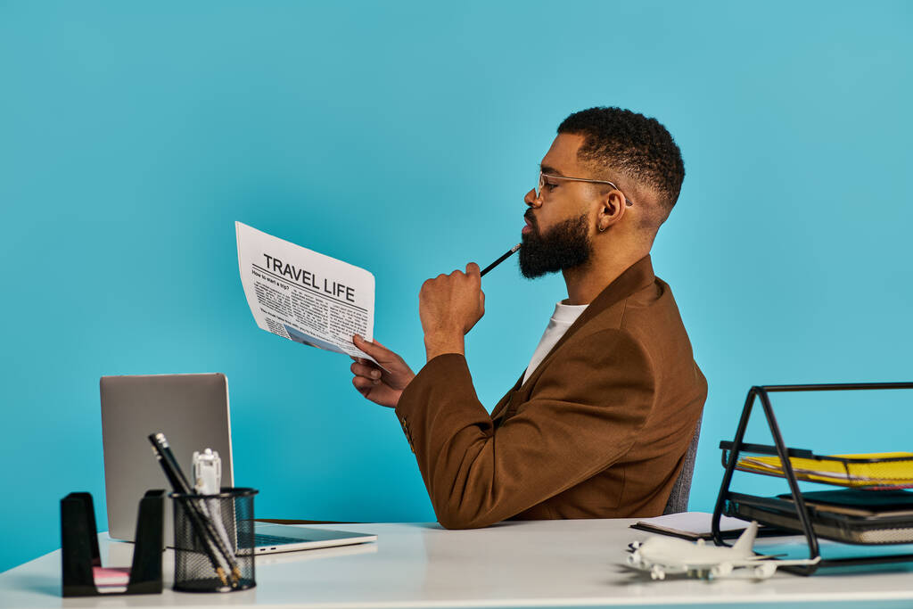 Um homem sentado numa secretária, envolvido na leitura de um jornal. Sua postura é focada e séria, pois absorve o conteúdo do documento. - Foto, Imagem