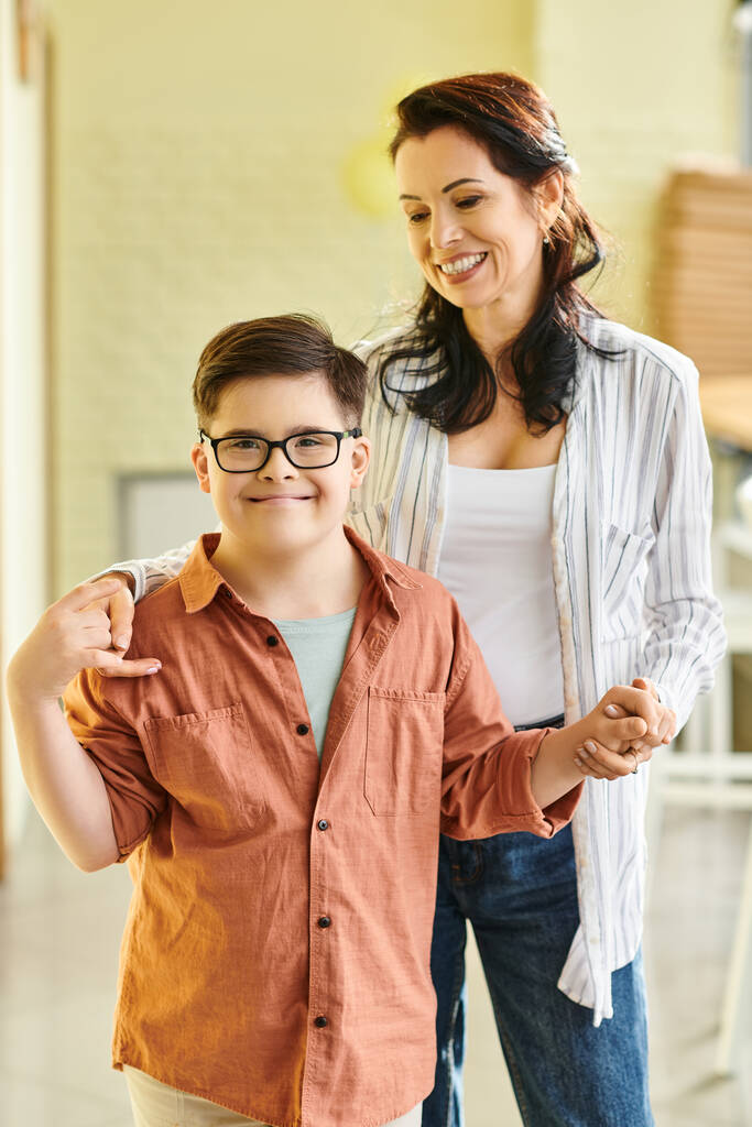 gelukkig tiener inclusieve jongen met Down syndroom poseren met zijn vrolijke moeder en glimlachen op camera - Foto, afbeelding