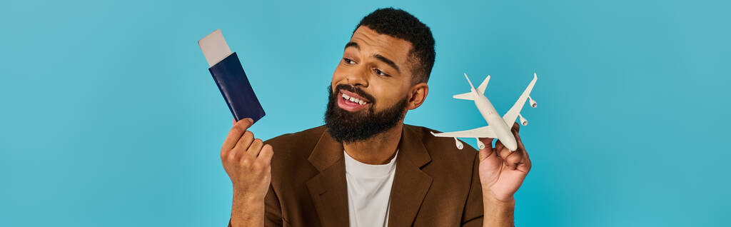 Mężczyzna trzyma w jednej ręce mały model samolotu, a w drugiej paszport, symbolizujący aspiracje podróżnicze i gotowość do przygody.. - Zdjęcie, obraz
