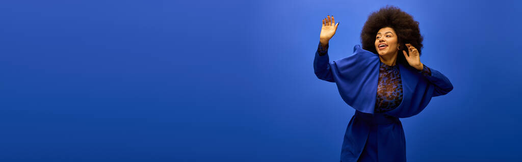 Femme afro-américaine élégante en robe bleue à la mode tient les mains vers le haut sur fond vibrant. - Photo, image