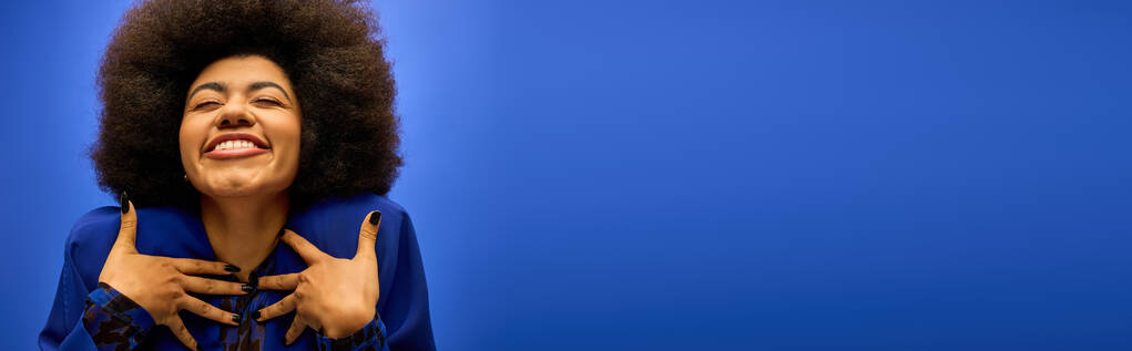 Mulher afro-americana elegante com penteado encaracolado parece calmo com as mãos descansando no peito. - Foto, Imagem