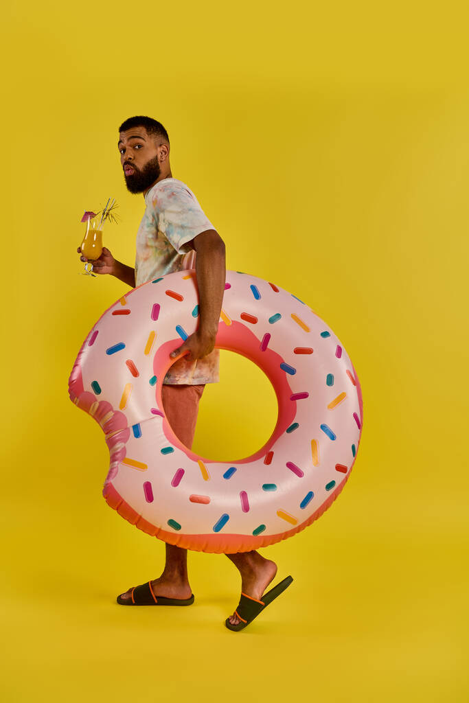Een man houdt vrolijk een gigantische donut in de ene hand en een glas bier in de andere, met een unieke en heerlijke combinatie van traktaties. - Foto, afbeelding