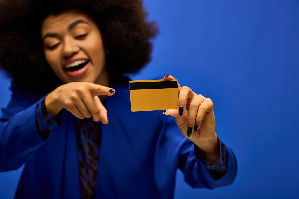 クレジットカードを指すトレンディな服装のスタイリッシュなアフリカ系アメリカ人女性. - 写真・画像
