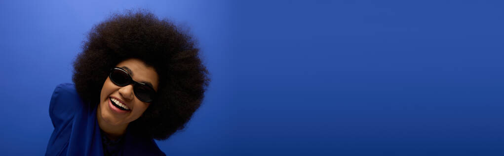 Stylowa Afroamerykanka pozuje w modnej niebieskiej kurtce i okularach przeciwsłonecznych. - Zdjęcie, obraz