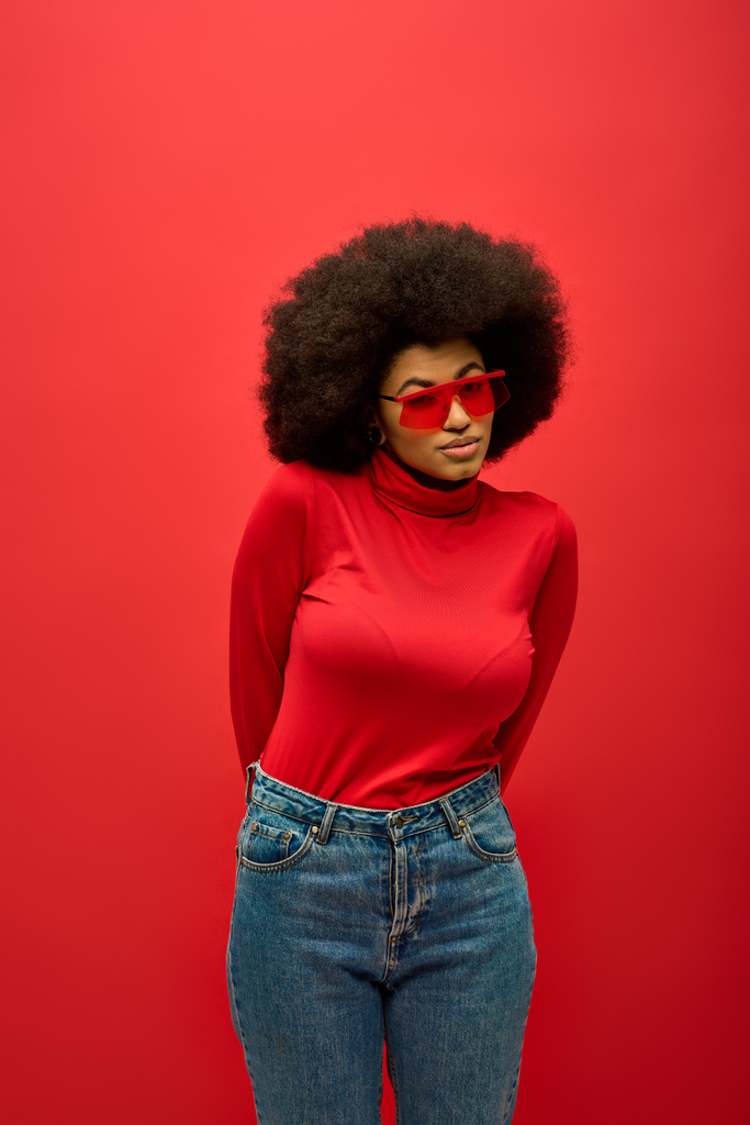 Afro-Amerikaanse vrouw poseren in trendy rode shirt en jeans tegen een levendige achtergrond. - Foto, afbeelding