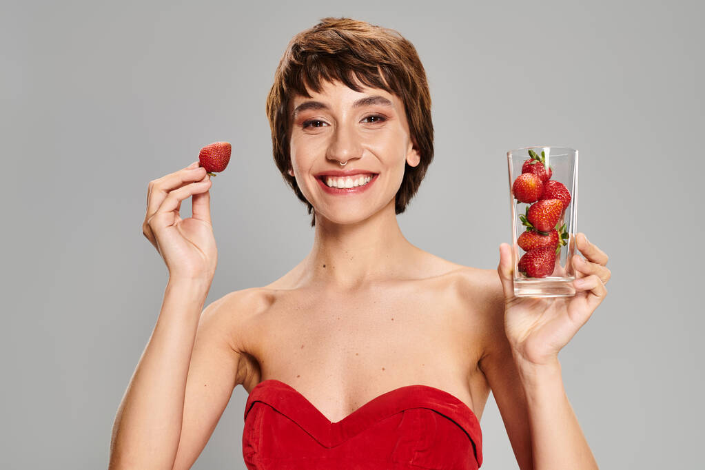 Mladá žena v červených šatech jemně drží sklenici jahod. - Fotografie, Obrázek