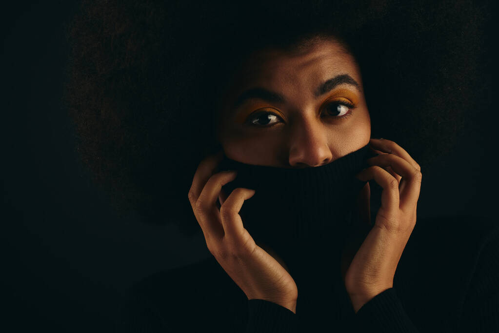 donna afroamericana copre con stile il viso con un panno nero sullo sfondo vibrante. - Foto, immagini