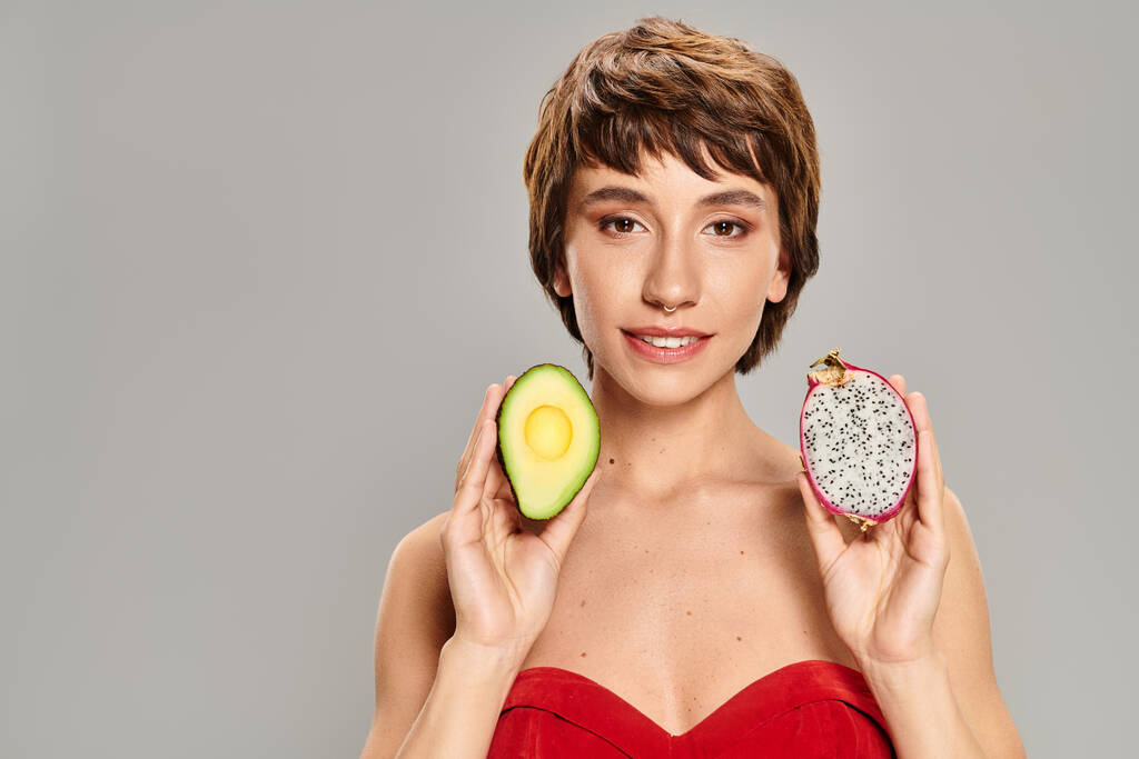 Young woman delicately holds an avocado and slice against vibrant backdrop. - Photo, Image