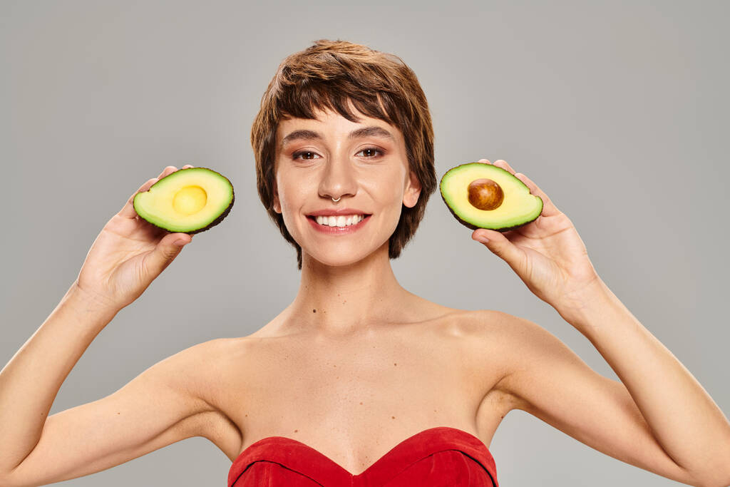 Eine junge Frau hält anmutig zwei Hälften einer Avocado. - Foto, Bild
