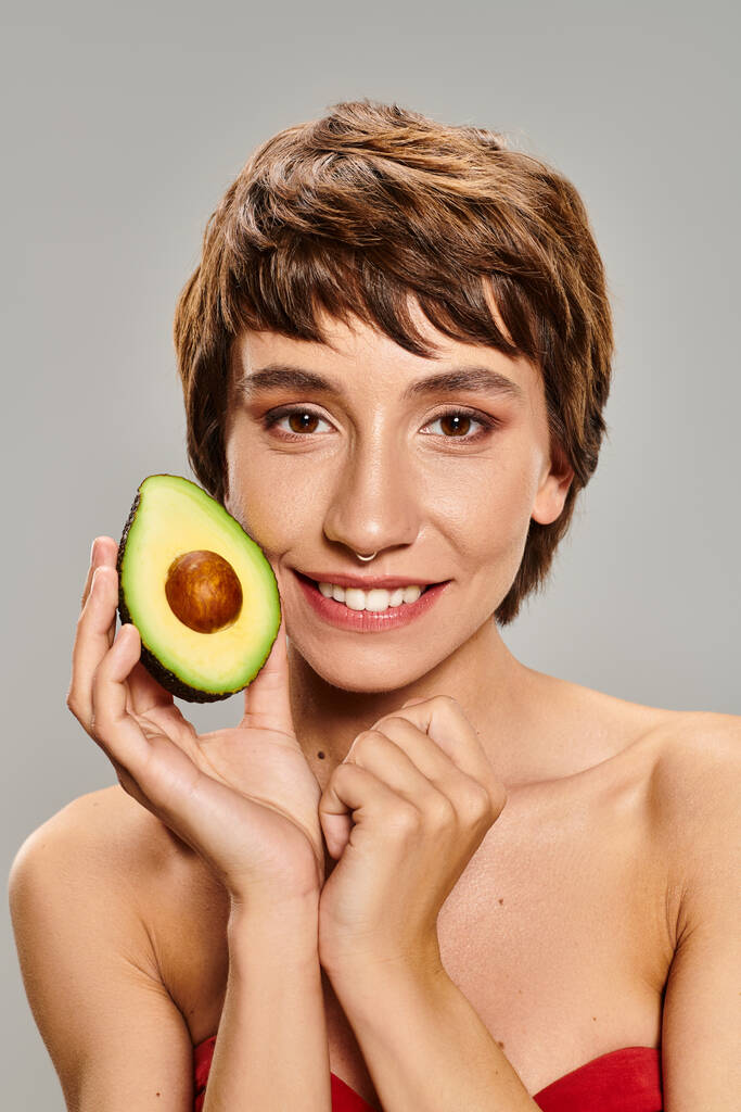 jonge vrouw houden avocado in voor haar gezicht. - Foto, afbeelding