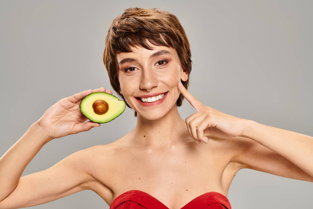 Eine Frau versteckt ihr Gesicht spielerisch hinter einer frischen Avocado. - Foto, Bild