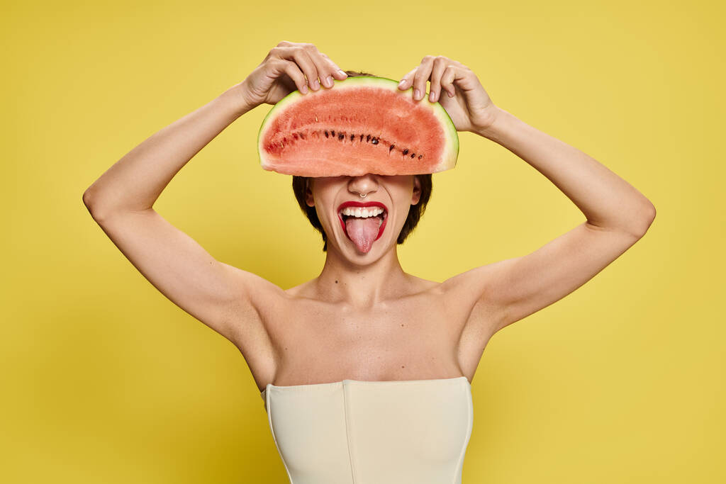 Une jeune femme équilibre un morceau de pastèque sur sa tête, entourée de couleurs vives. - Photo, image