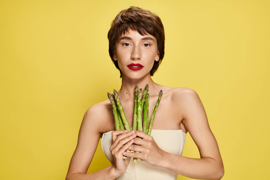 Una giovane donna che tiene un mucchio di asparagi davanti al viso. - Foto, immagini