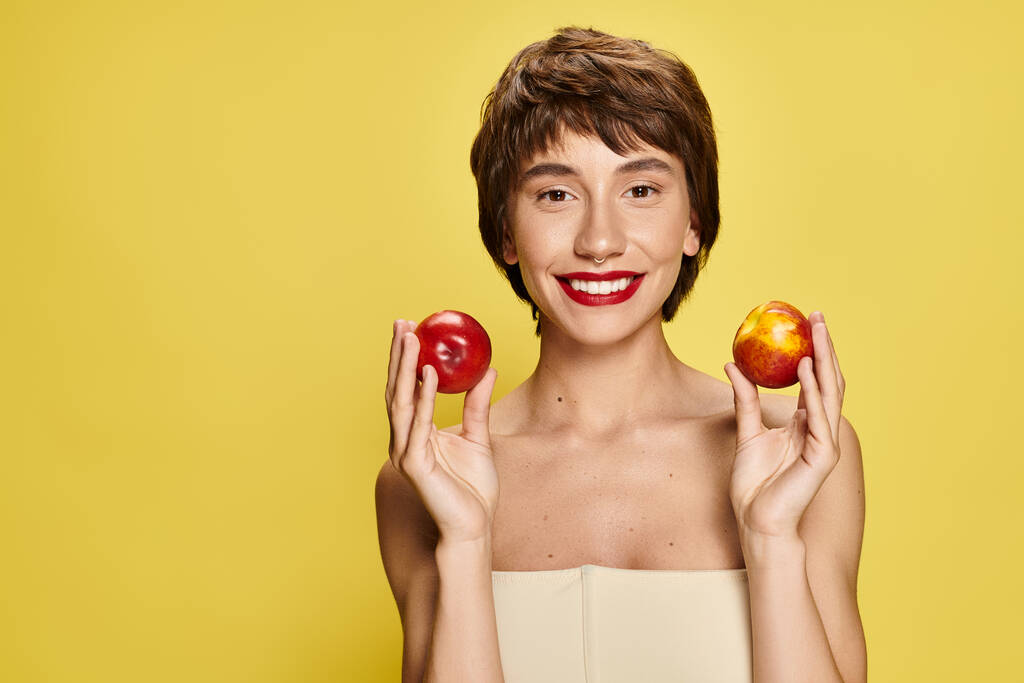 Eine junge Frau hält zwei Pfirsiche mit einer vor dem Gesicht. - Foto, Bild