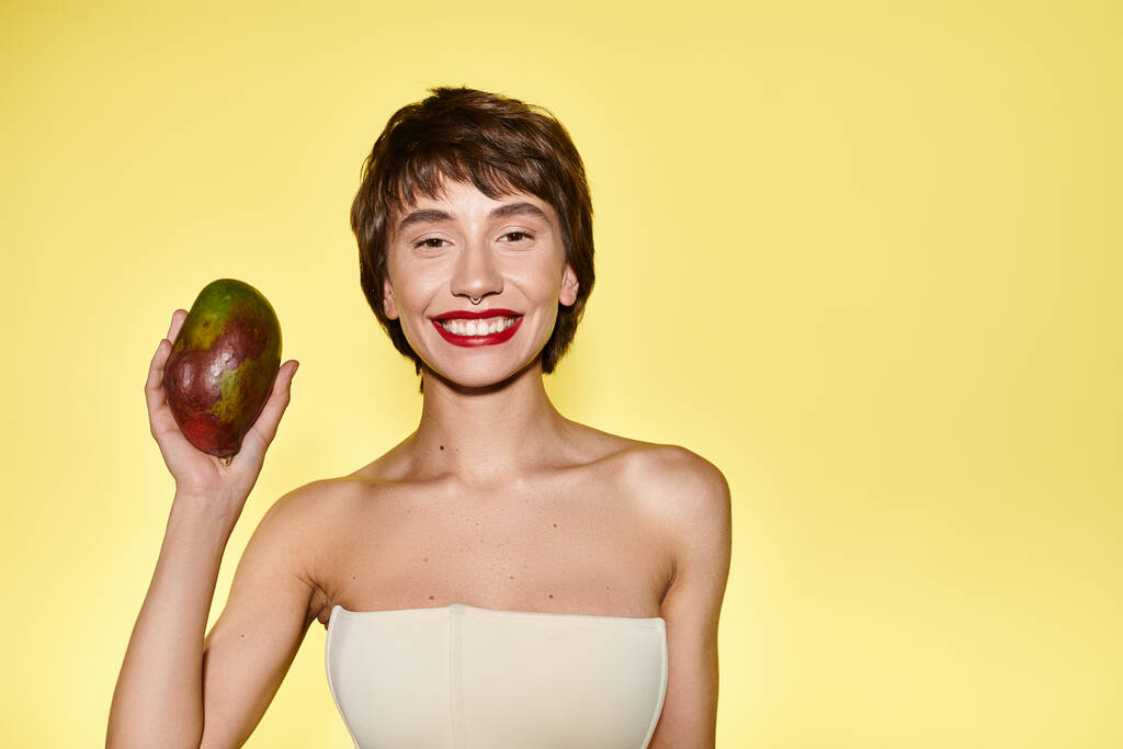 Een jonge vrouw in een witte jurk houdt mango, tegen een levendige achtergrond. - Foto, afbeelding