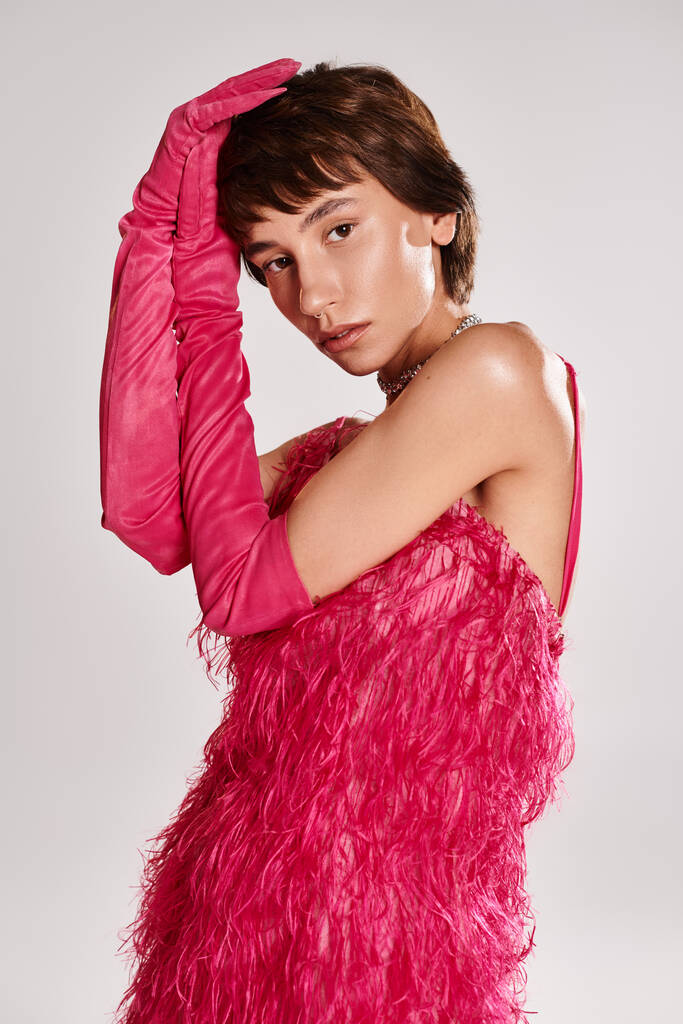 Fashionable young woman striking pose in vibrant pink feather dress. - Photo, Image